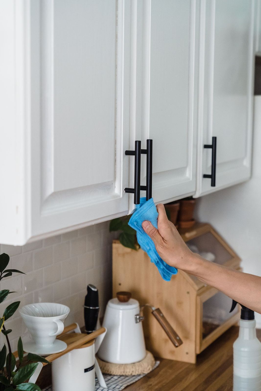 A cleaner wiping down bright white kitchen cabinet doors with a cloth