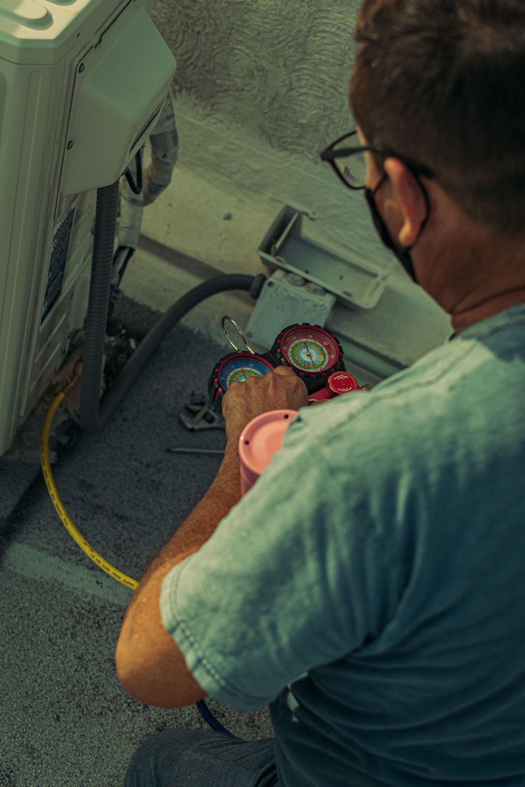 Technician reading refrigerant gauges while servicing an outdoor AC unit